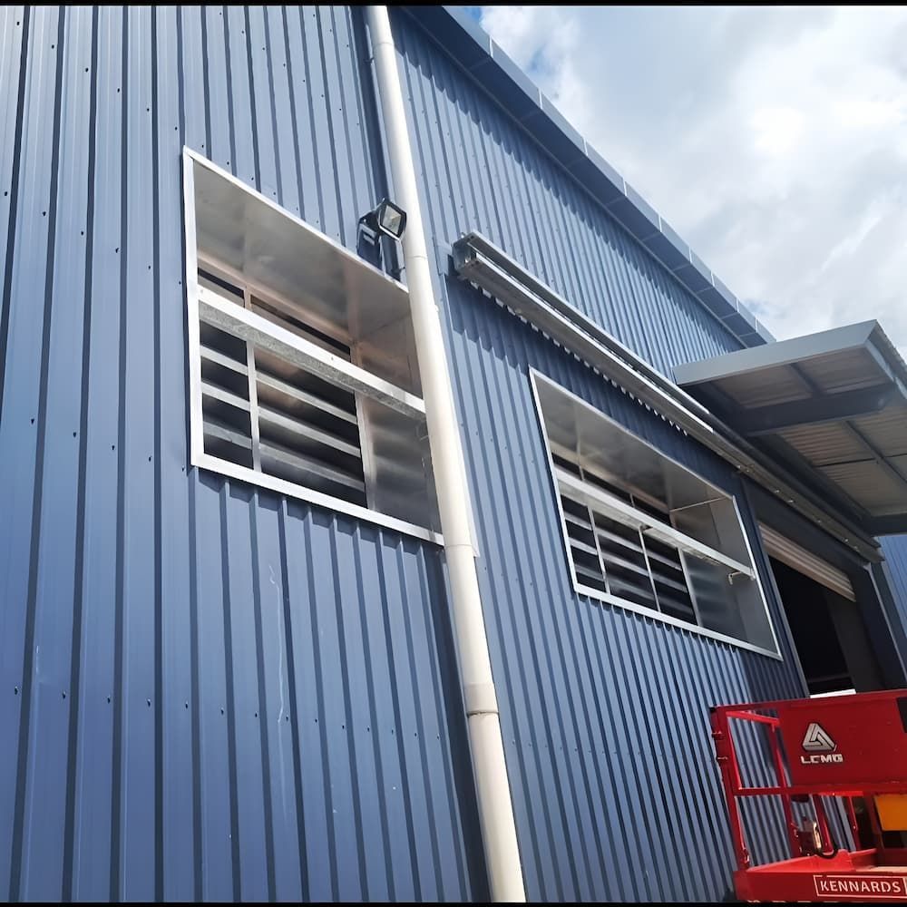 Blue Corrugated Metal Building With Barred Windows and White Gutter — KNG Roofing And Construction in Borroloola, NT