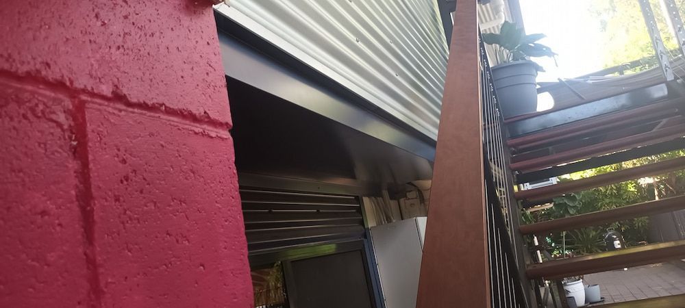 Red Brick Wall Next to a Metal Roller Shutter — KNG Roofing And Construction in Darwin, NT