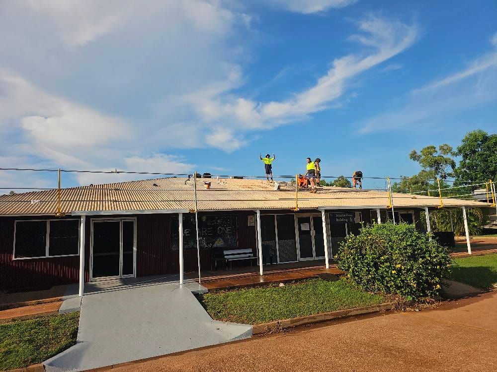 Construction Workers on a Building Roof Under a Blue Sky — KNG Roofing And Construction in Darwin, NT