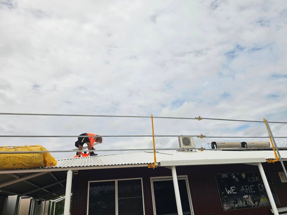 A Worker on a Rooftop With Safety Equipment, Under a Cloudy Sky — KNG Roofing And Construction in Darwin, NT