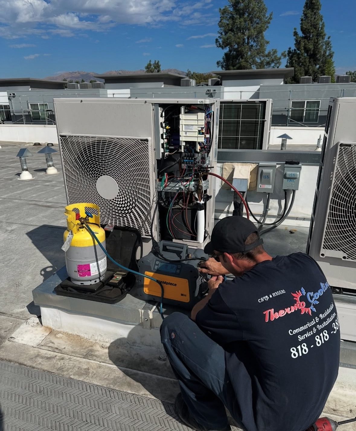 HVAC technician working on rooftop air conditioning unit, yellow gas tank nearby.