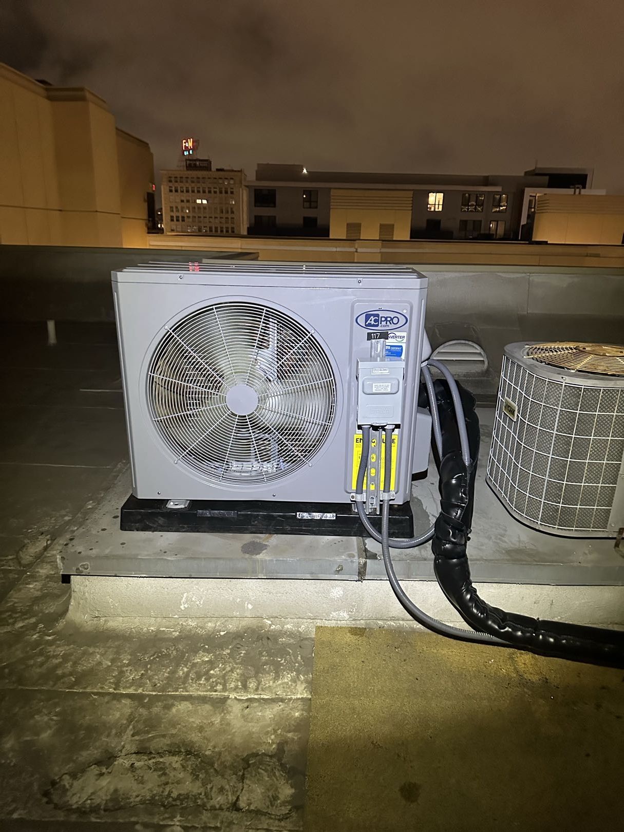 Person in black shirt and cap cleaning air conditioner filter on white wall.