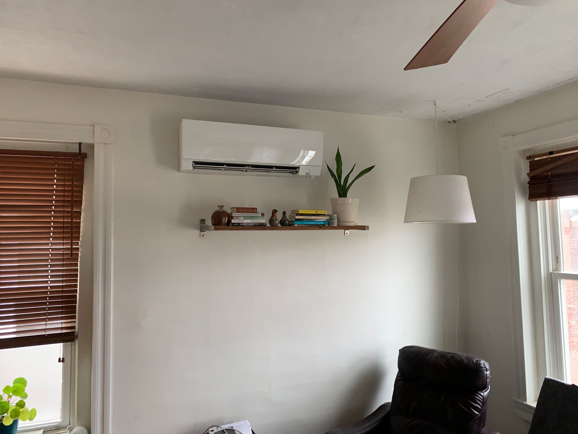 White wall with air conditioner, shelf, lamp, and window with blinds.