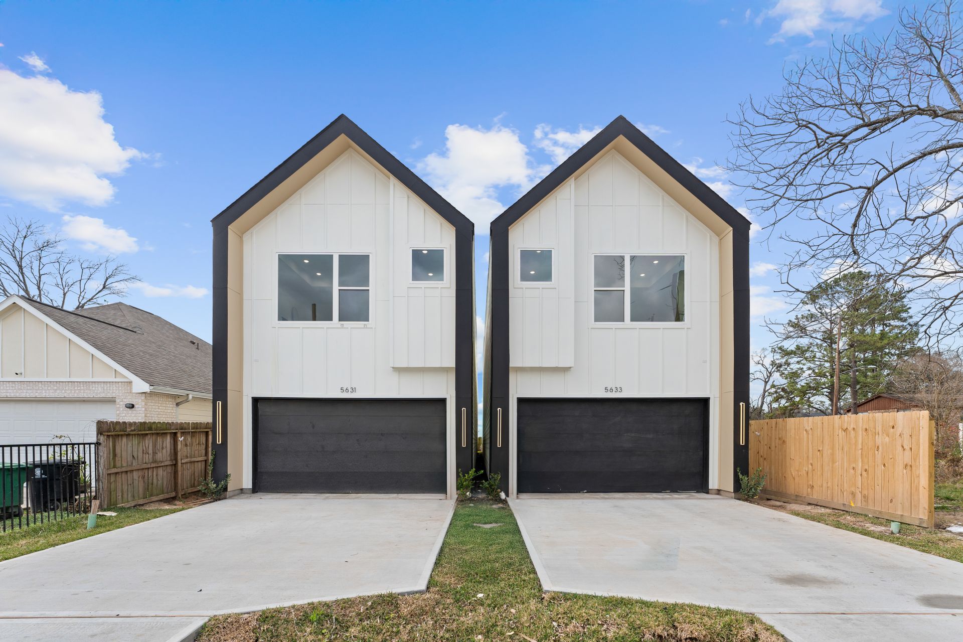 Two modern white townhouses with black accents and garage doors, blue sky background.