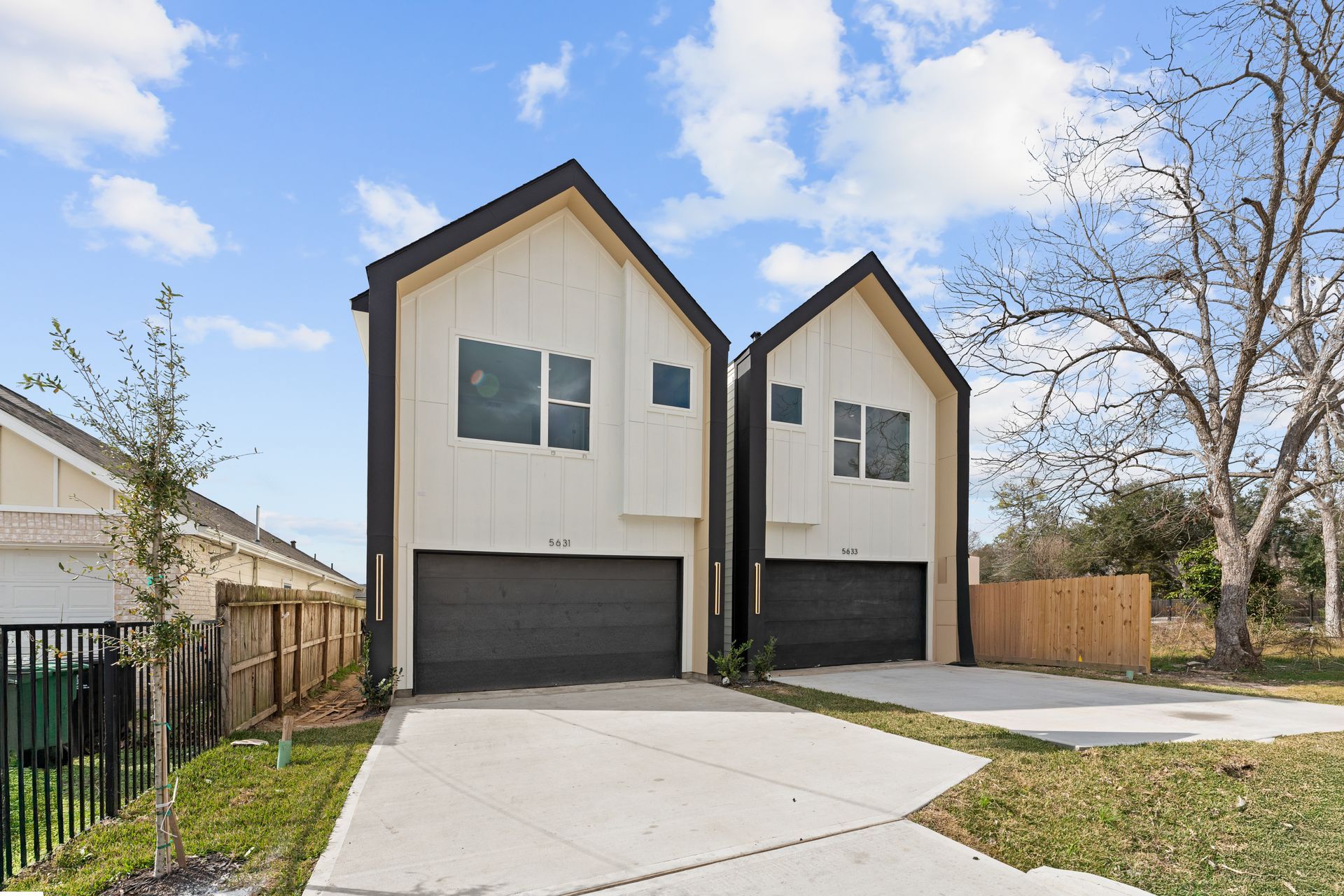 Two modern townhomes with gray garage doors, concrete driveways, and blue skies.