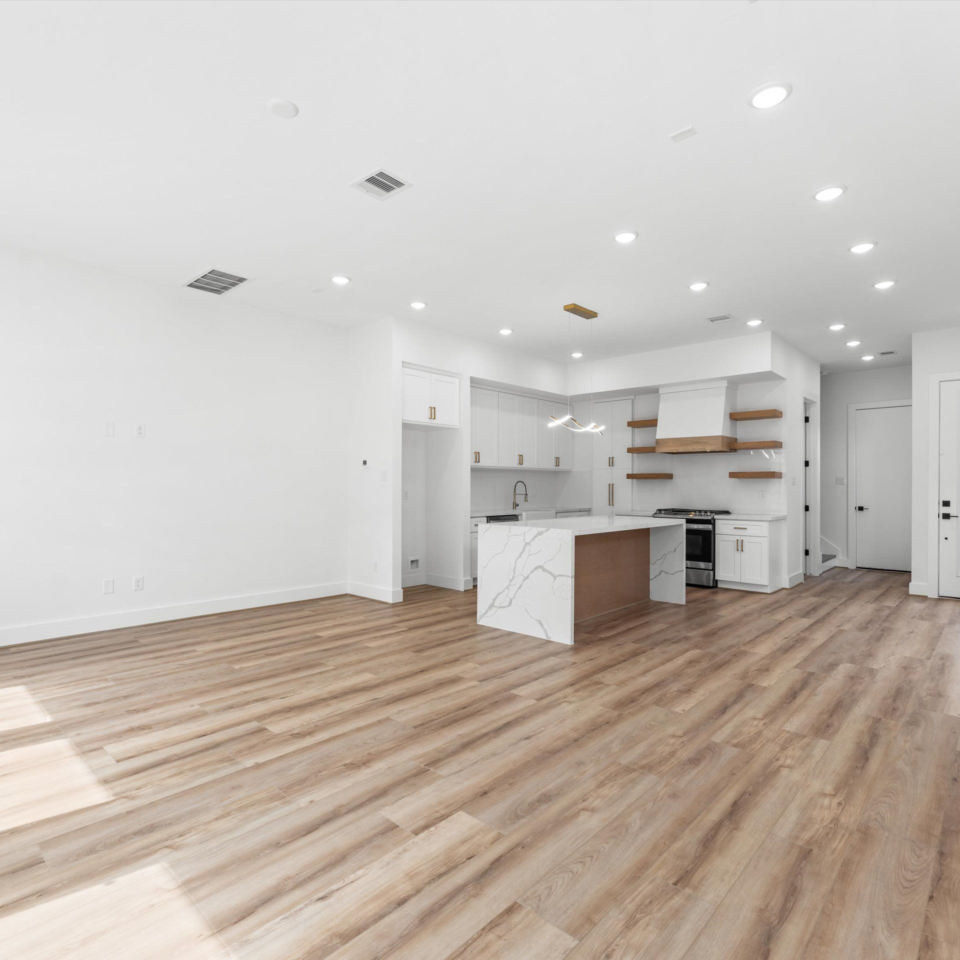 Empty, bright kitchen with a quartz island and wooden floors. White cabinets and walls, modern design.