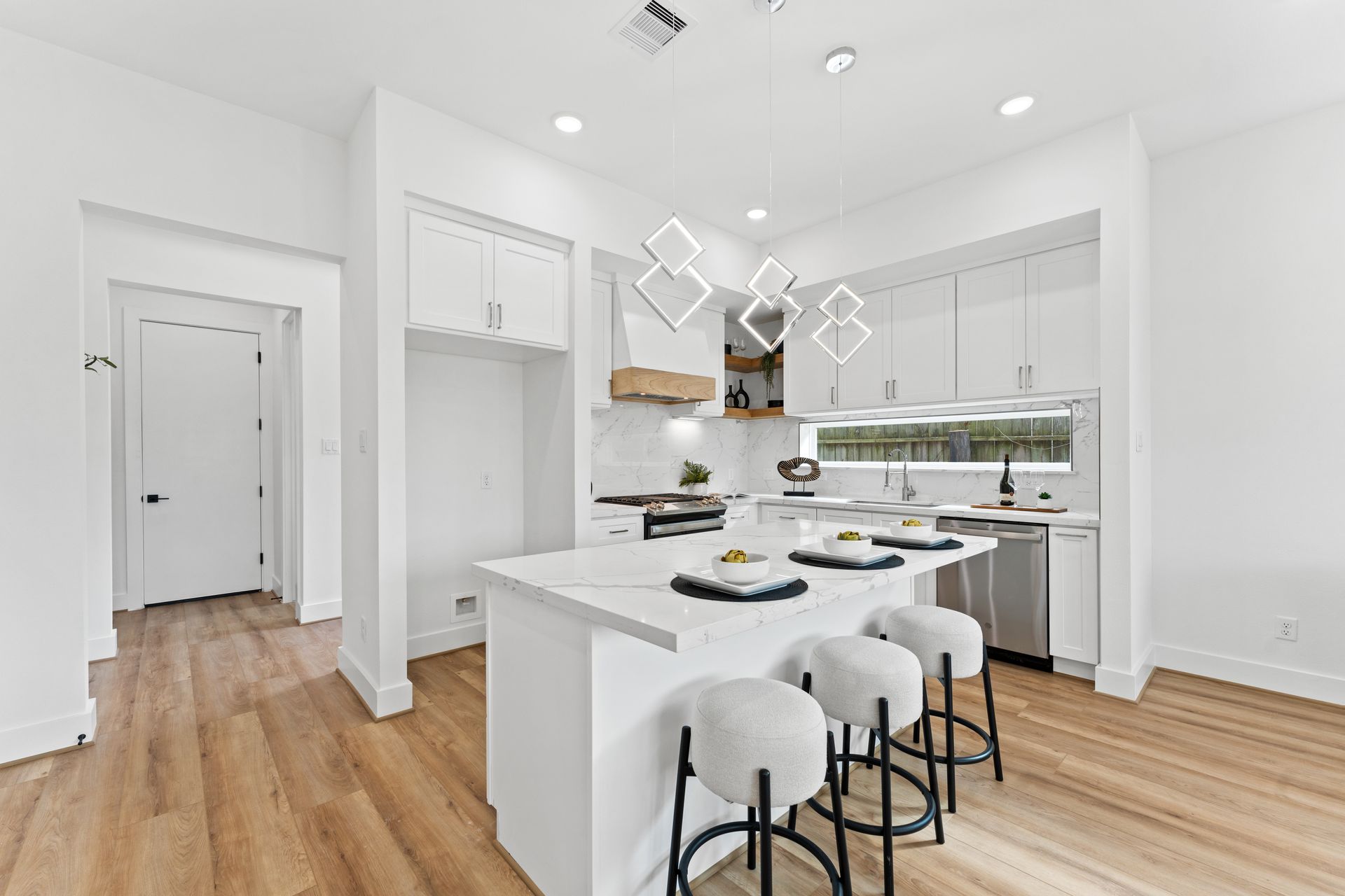 Modern white kitchen with island, three bar stools, and light wood floors.