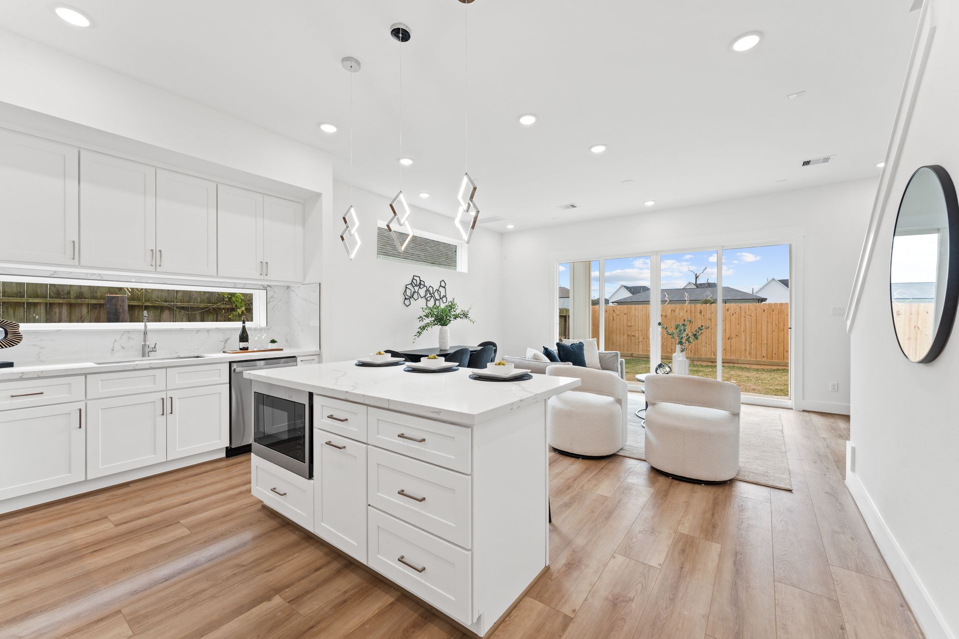 Modern white kitchen with island, stainless steel appliances, and a view to the backyard.