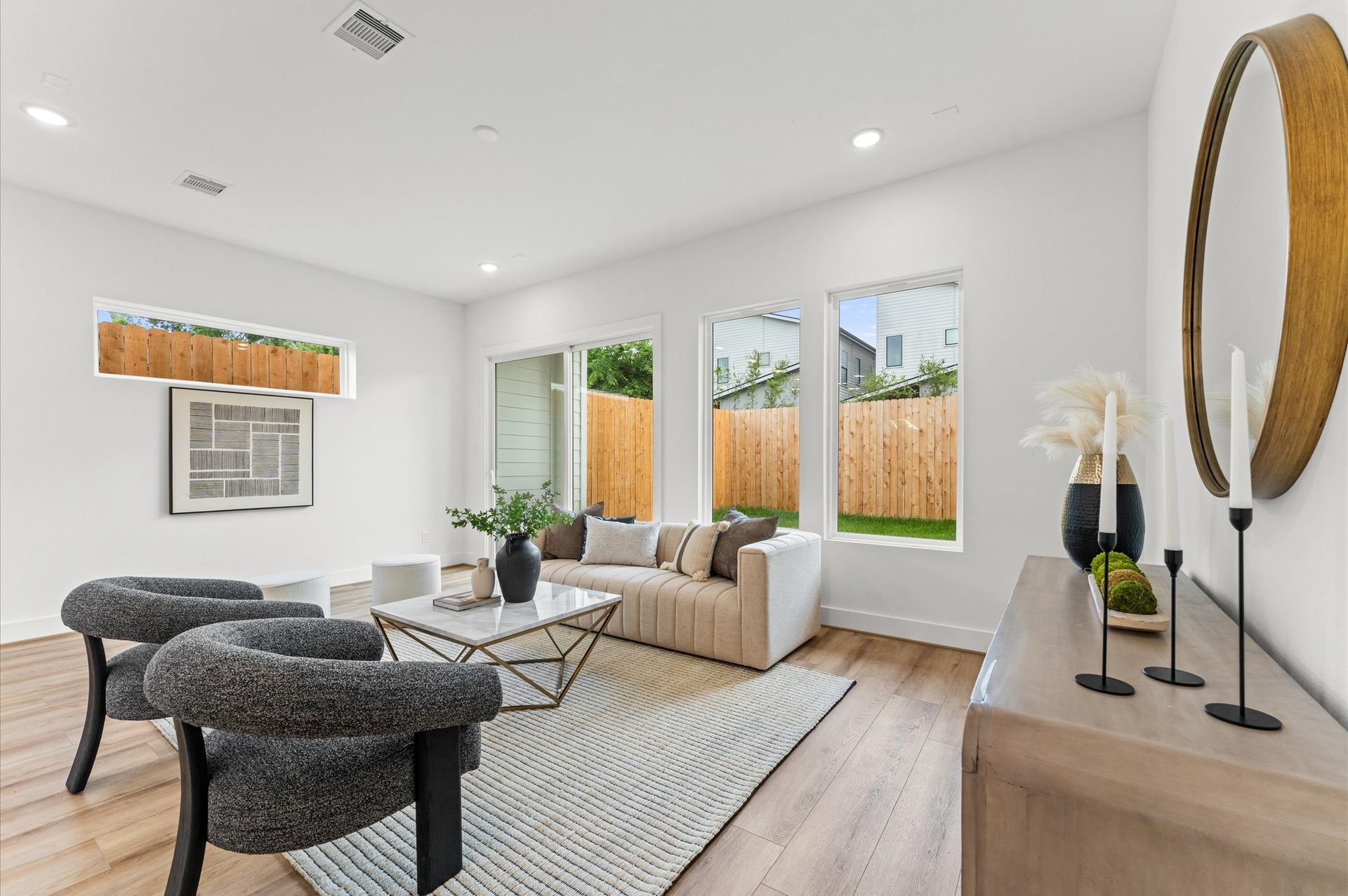 Modern living room with neutral tones, sofa, chairs, rug, and large windows.