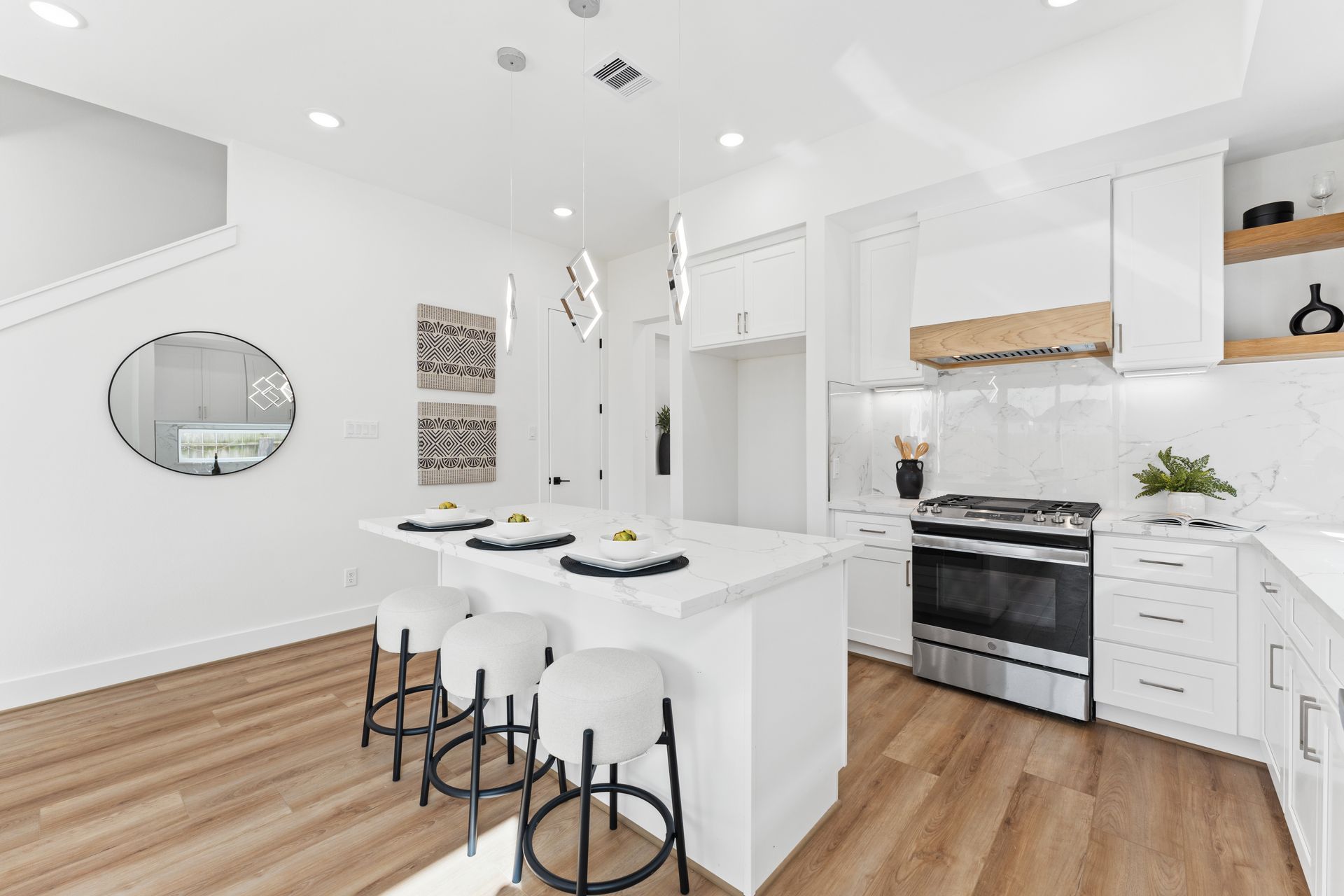 Modern white kitchen with island seating, stainless steel appliances, and wood accents.