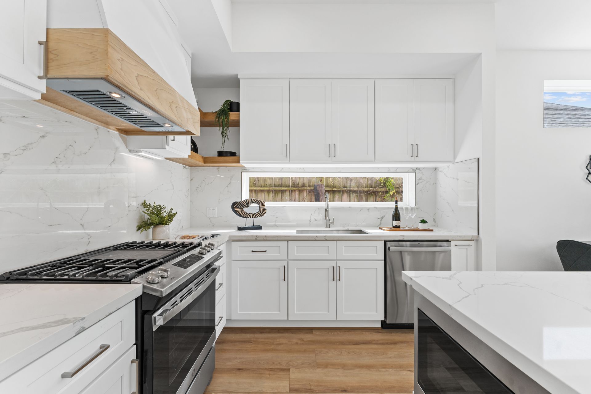 Modern white kitchen with marble countertops, stainless steel appliances, and wood accents.