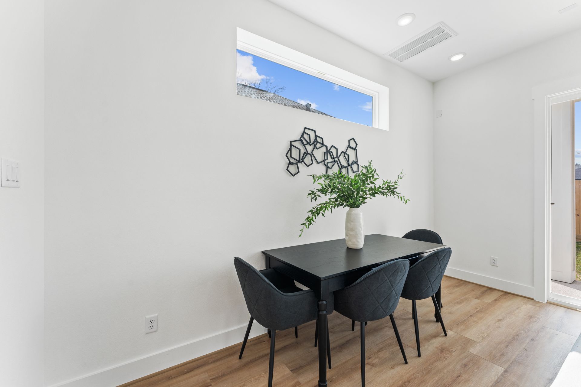 Dining area with black table and chairs, white walls, and a decorative plant.