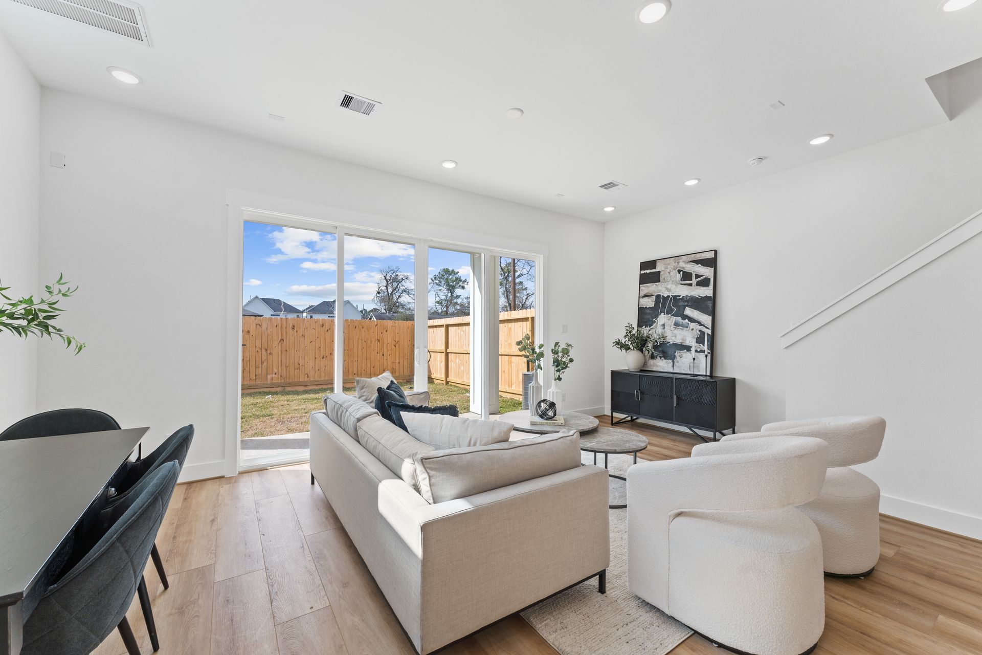 Bright living room with light wood floors, white walls, and large sliding glass door to backyard.