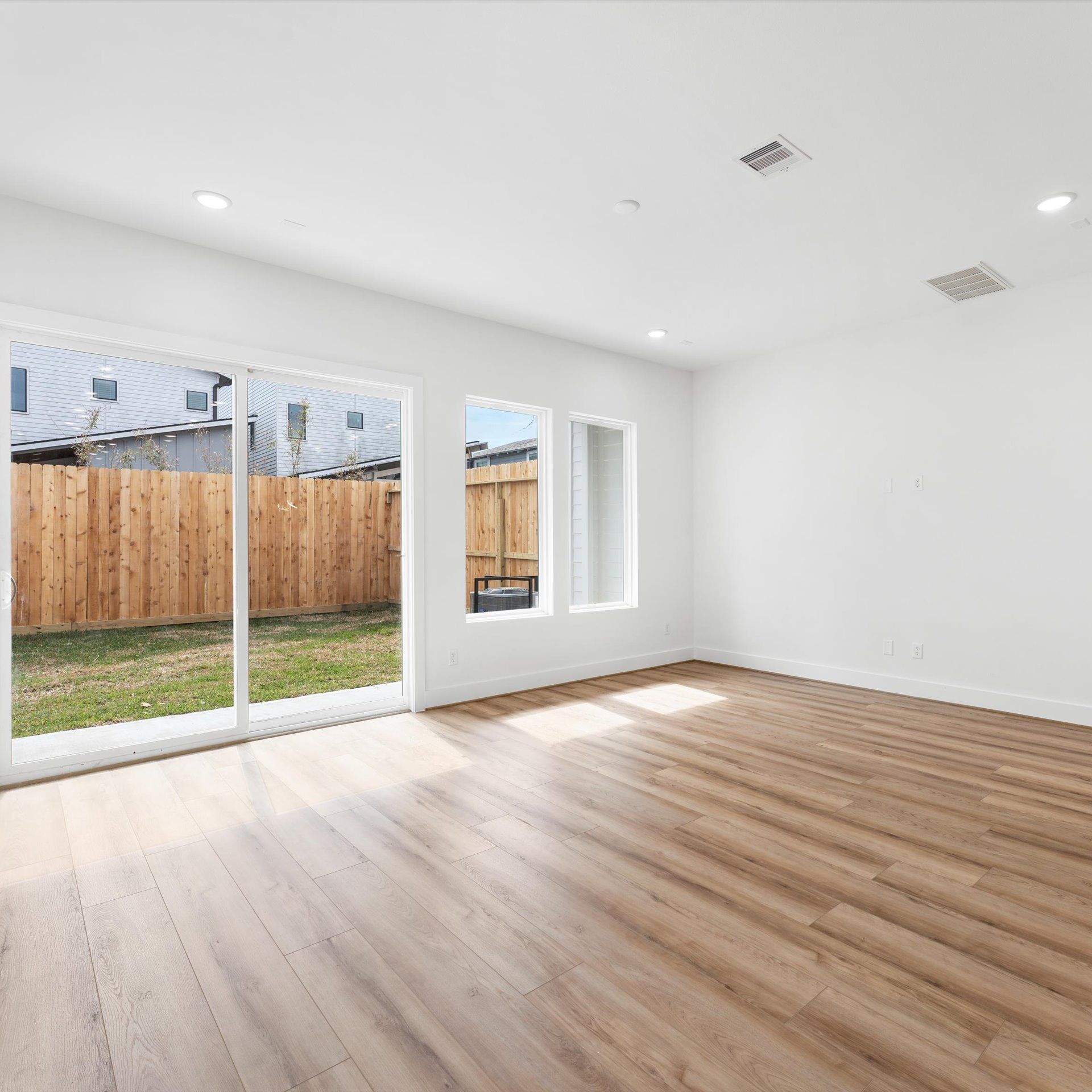 Empty room with wood floors, sliding glass door to fenced yard, and white walls.