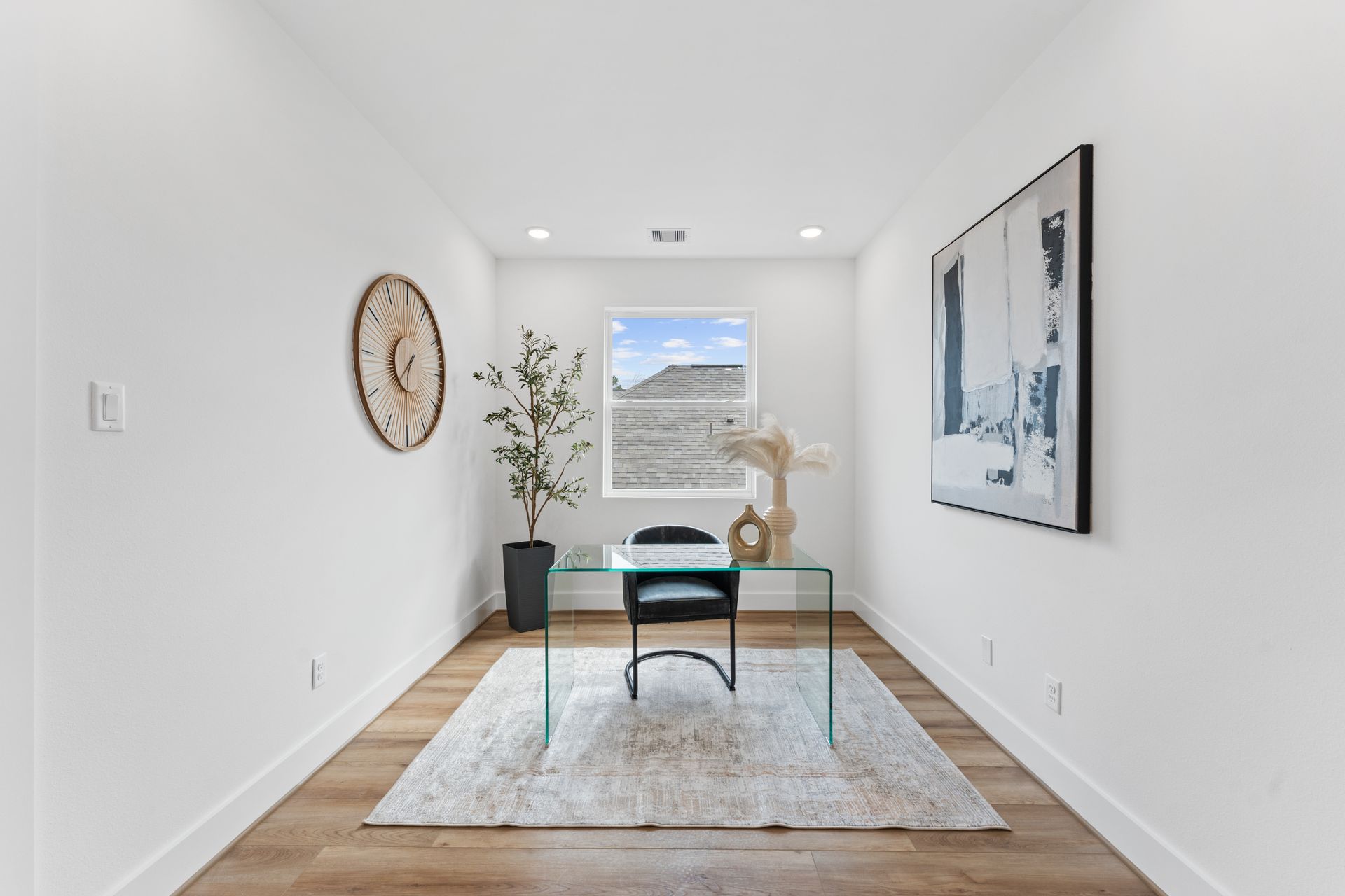 Home office with glass desk, neutral decor, and a window offering a view.