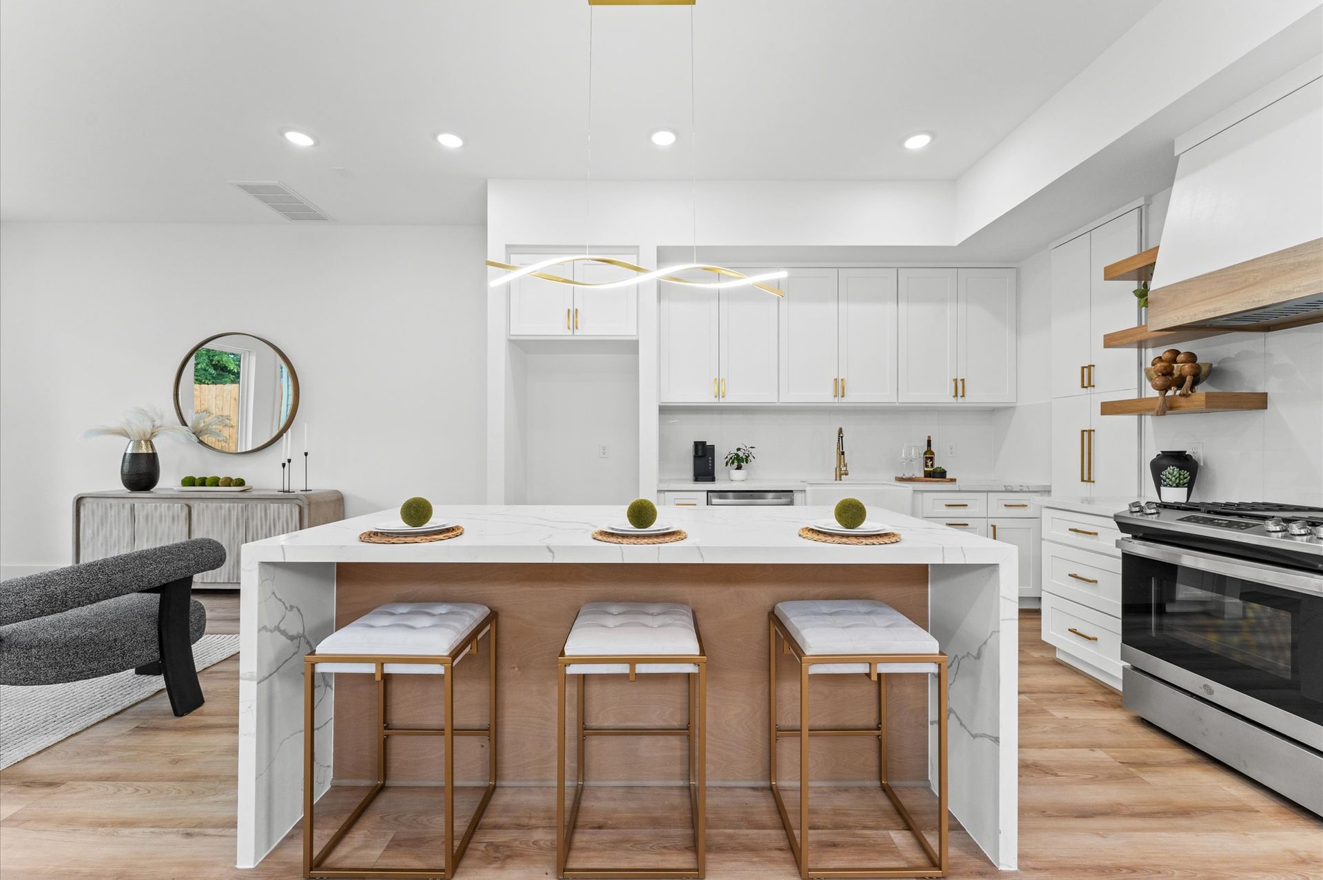 Modern white kitchen with island, gold accents, and breakfast stools.