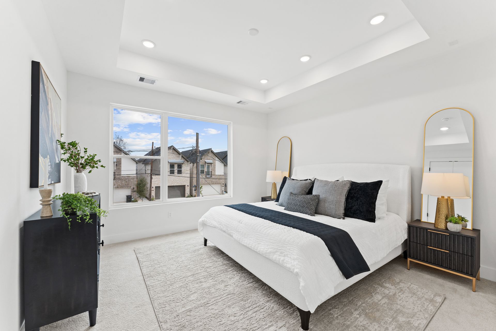 Modern bedroom with a bed, black dresser, and a large window overlooking other homes.