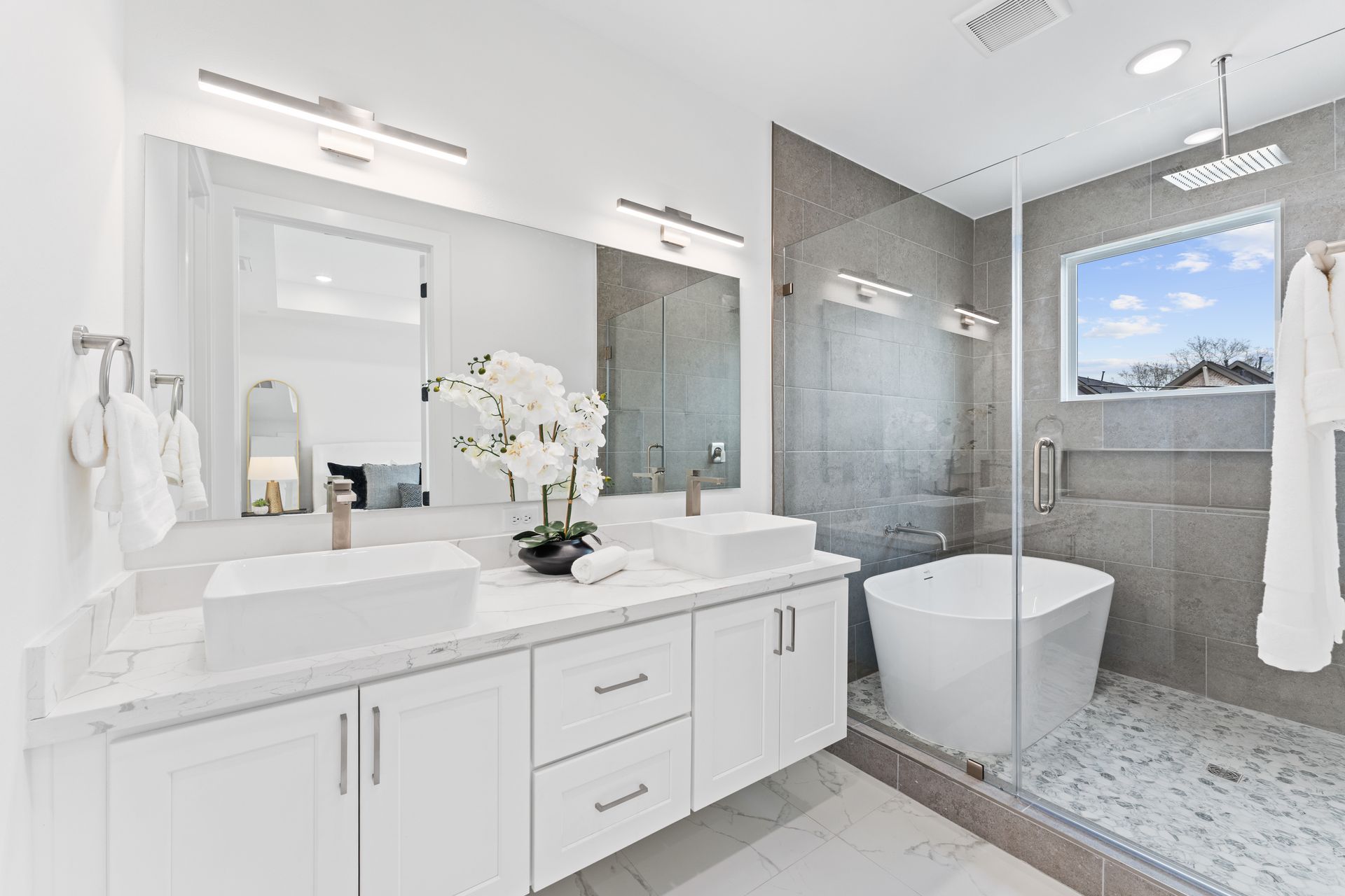 Modern white bathroom with double vanity, soaking tub, and glass shower.