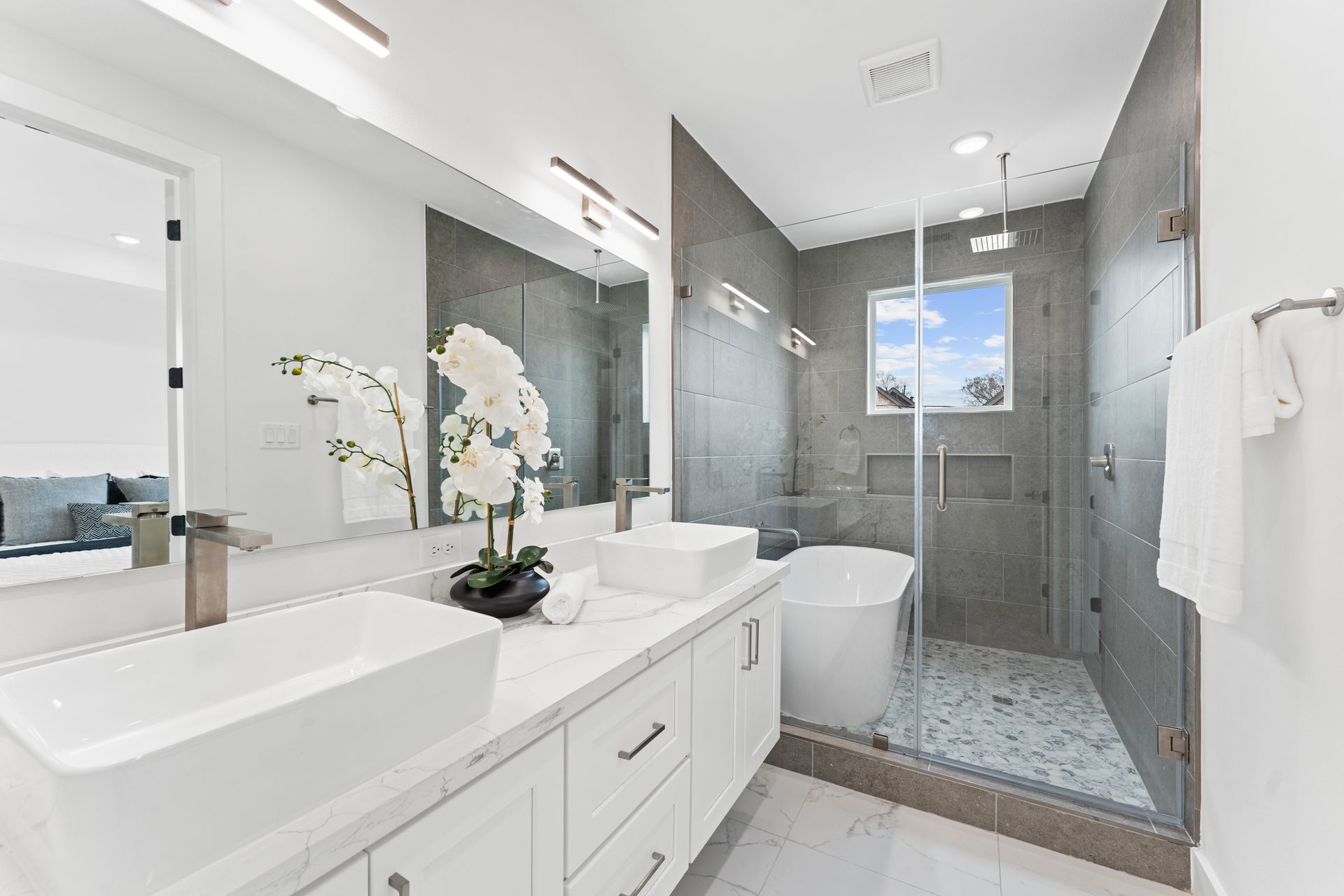 Modern bathroom with double sinks, a shower, and a freestanding tub. Light gray and white color scheme.