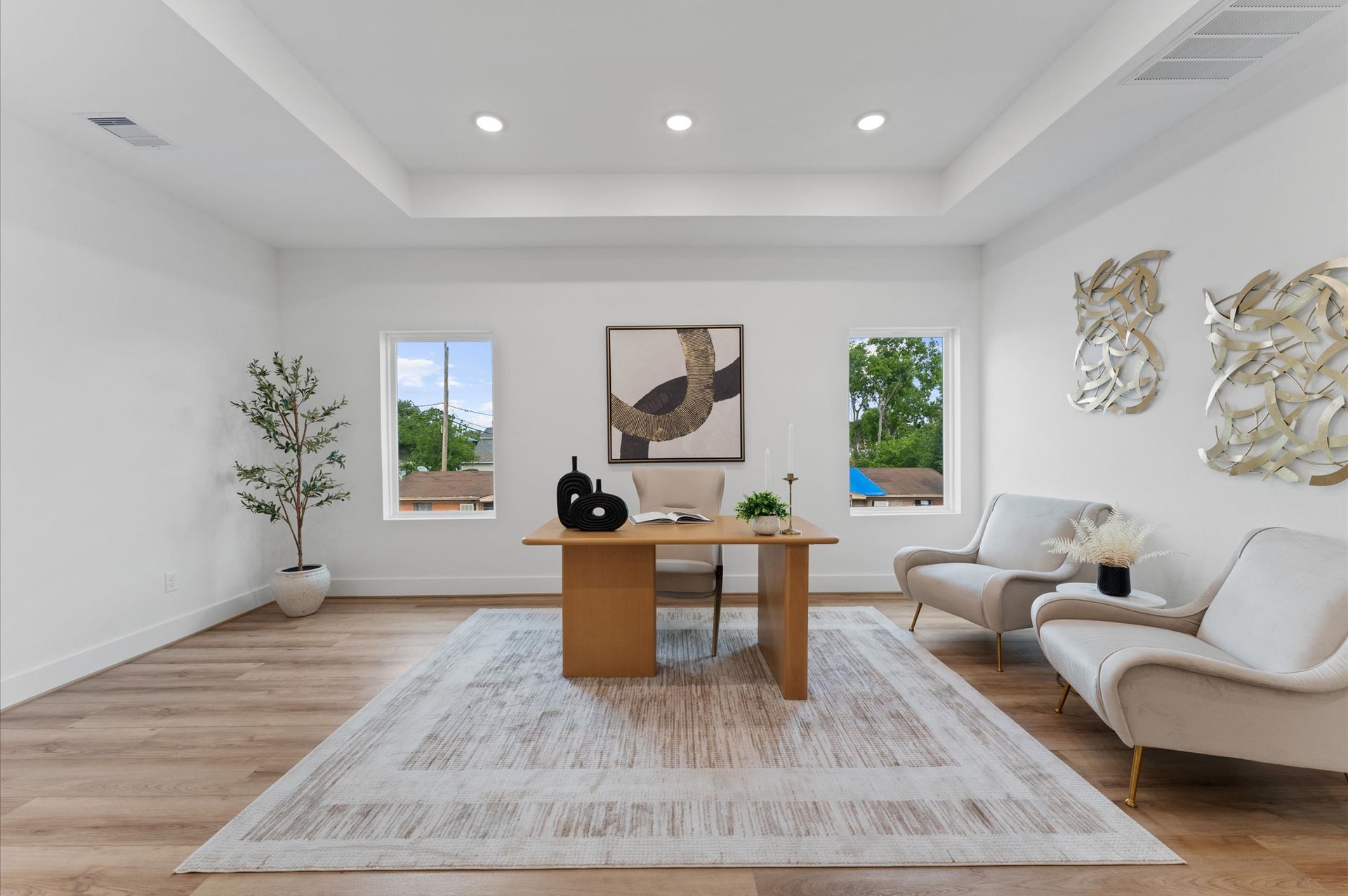 Modern home office with light wood desk, rug, and two armchairs. White walls and ceiling, with artwork.