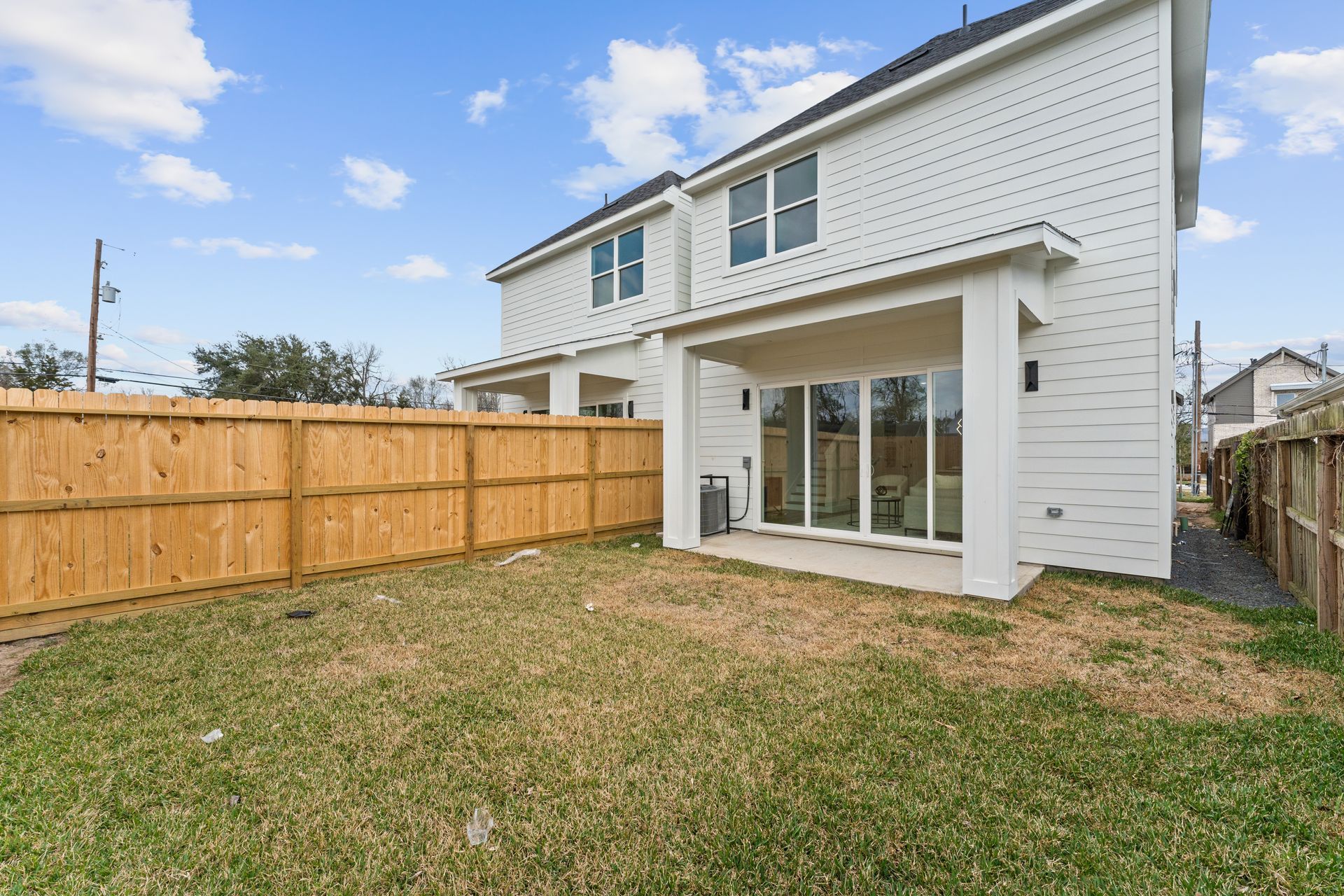 Backyard with wooden fence, grass, and a white house with a covered patio and sliding glass doors.