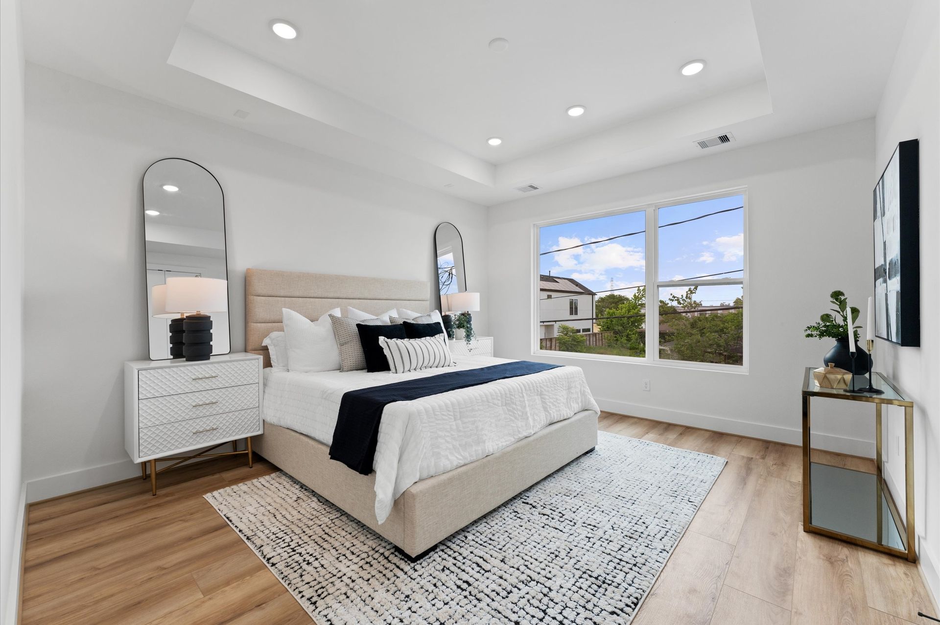 Bright bedroom with a bed, mirrors, nightstands, and a large window overlooking greenery.