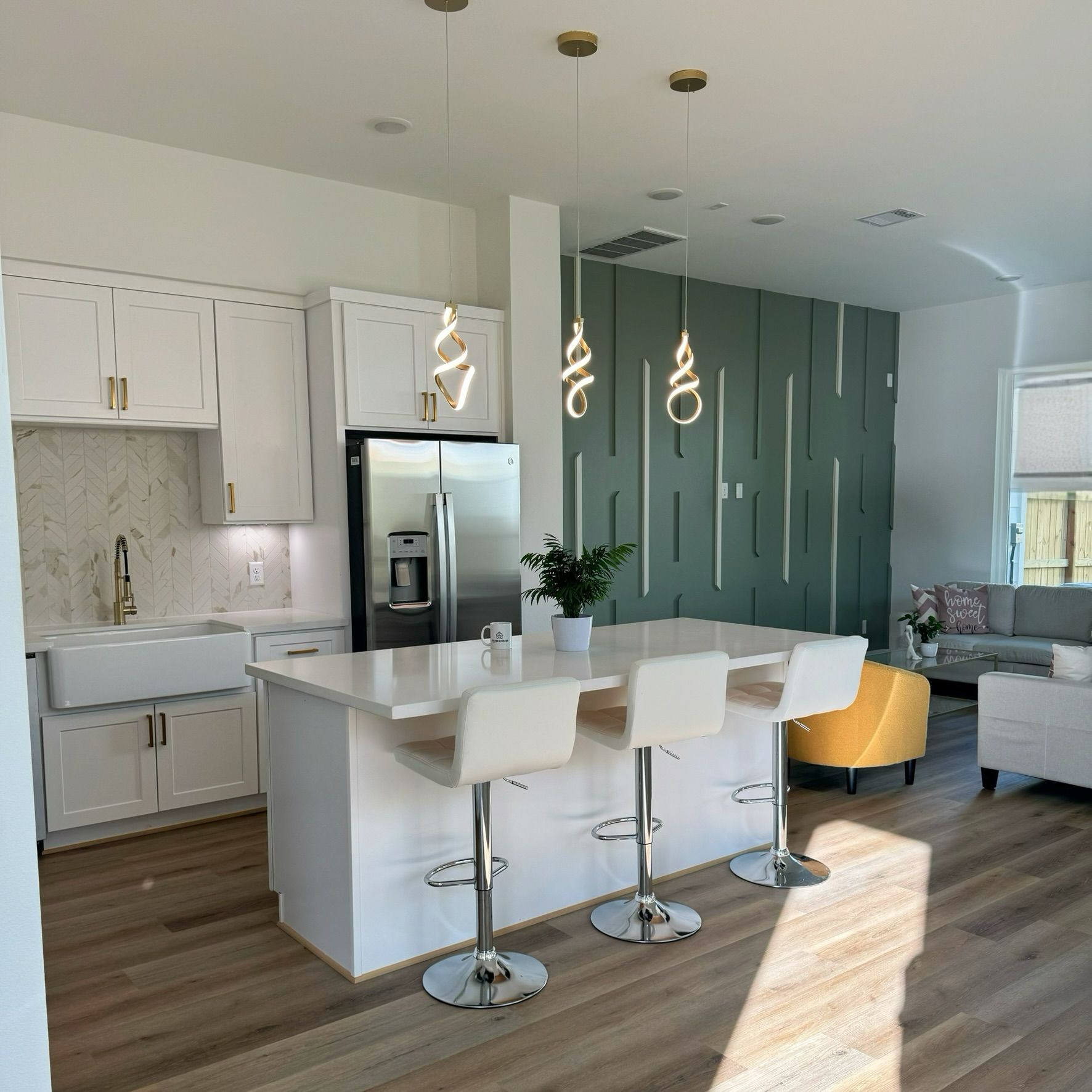 Modern kitchen with white cabinets, island, and light fixtures; green accent wall; and hardwood floors.