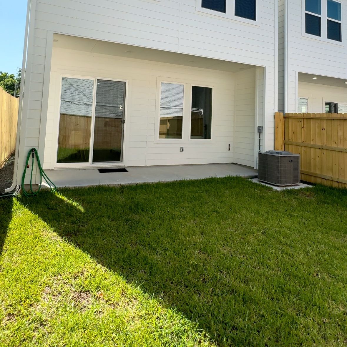 Backyard of a white house with a patio, green grass, and a wooden fence.