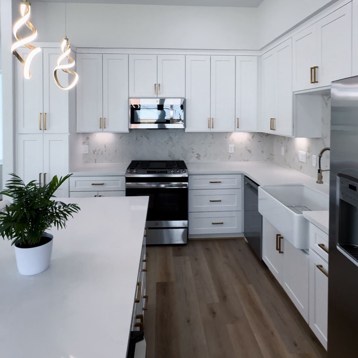 Modern white kitchen with island, stainless steel appliances, and hardwood floors.