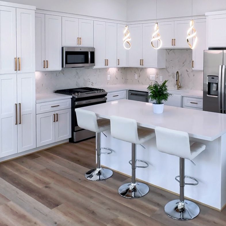 White kitchen with an island, white cabinets, and stainless steel appliances; three bar stools.