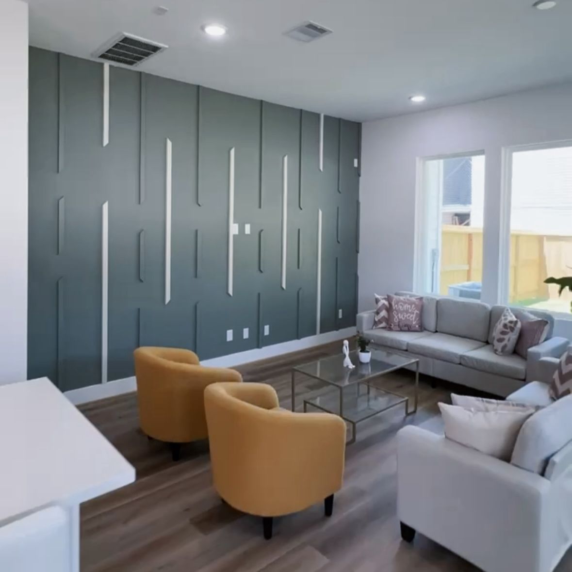 Modern living room with gray accent wall, mustard chairs, and two white sofas.