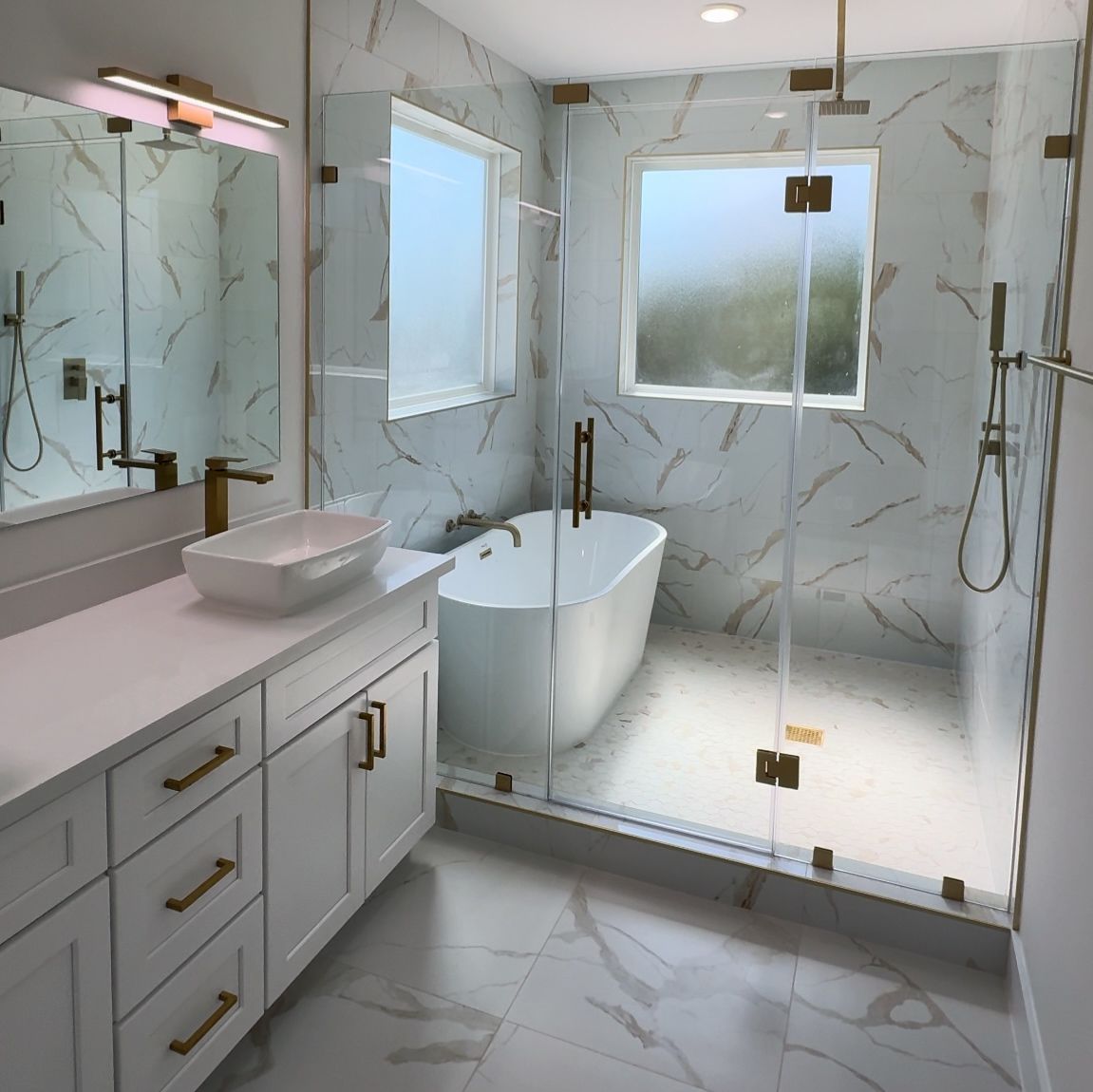 Modern bathroom with white vanity, marble walls, freestanding tub, and glass shower.
