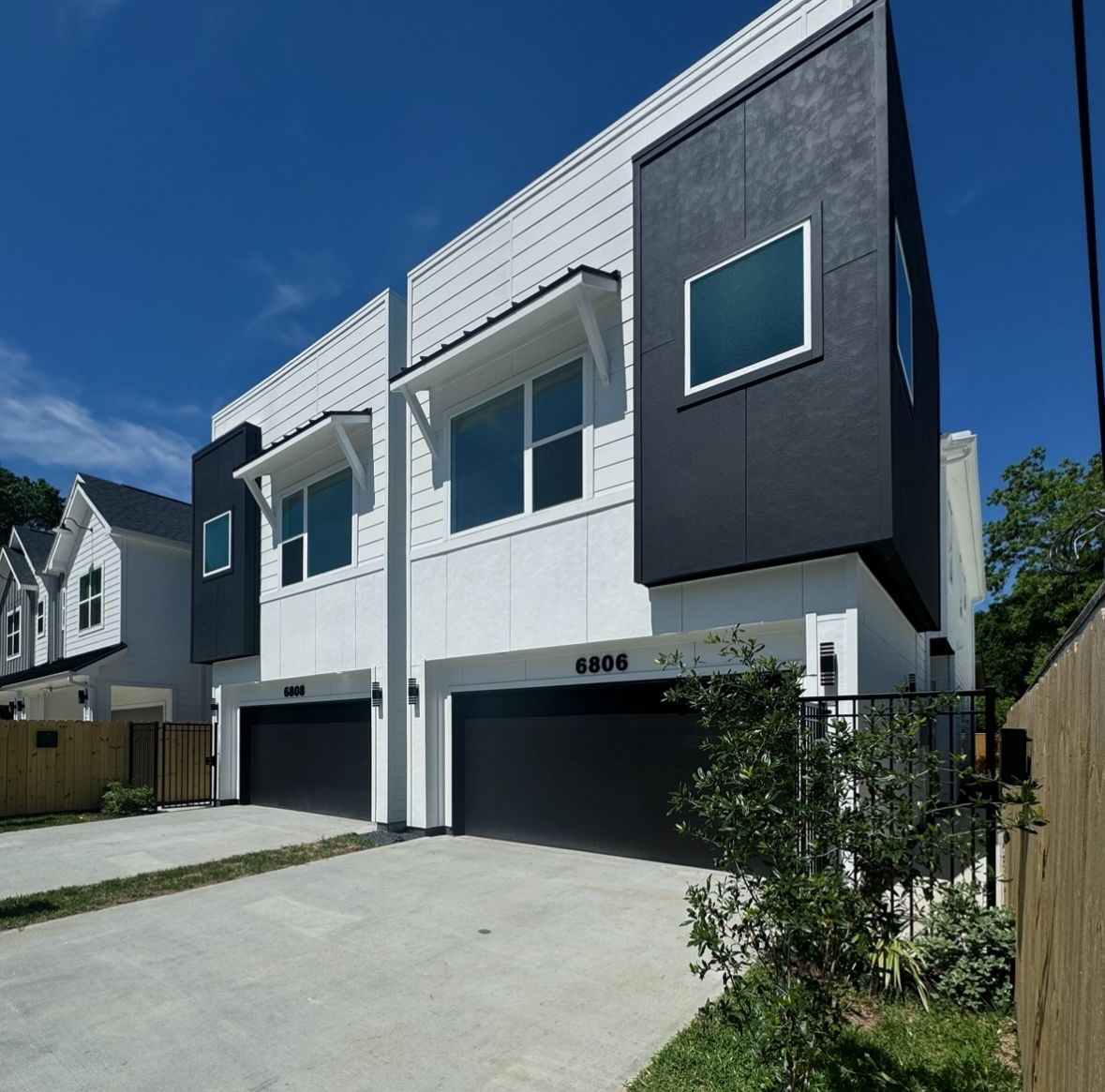 Modern white and black townhomes with garage doors. Blue sky in the background.