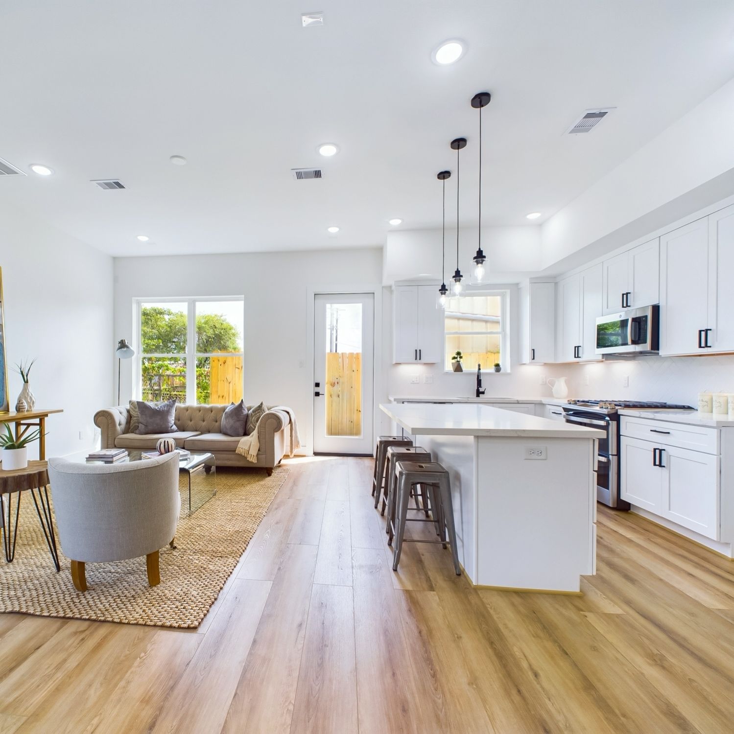 Open-concept kitchen and living room with white cabinets, light wood floors, and island with stools.