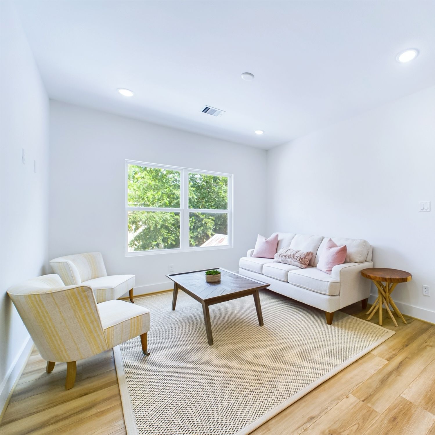Bright living room with white walls, light wood floors. Furnishings include a sofa, two chairs, a coffee table.