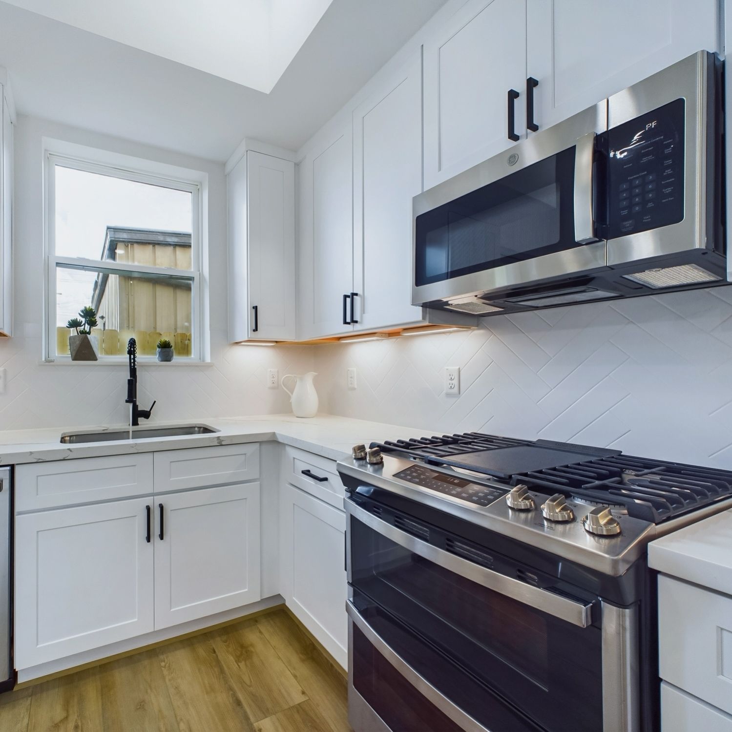 White kitchen with stainless steel appliances, white cabinets, and a window.