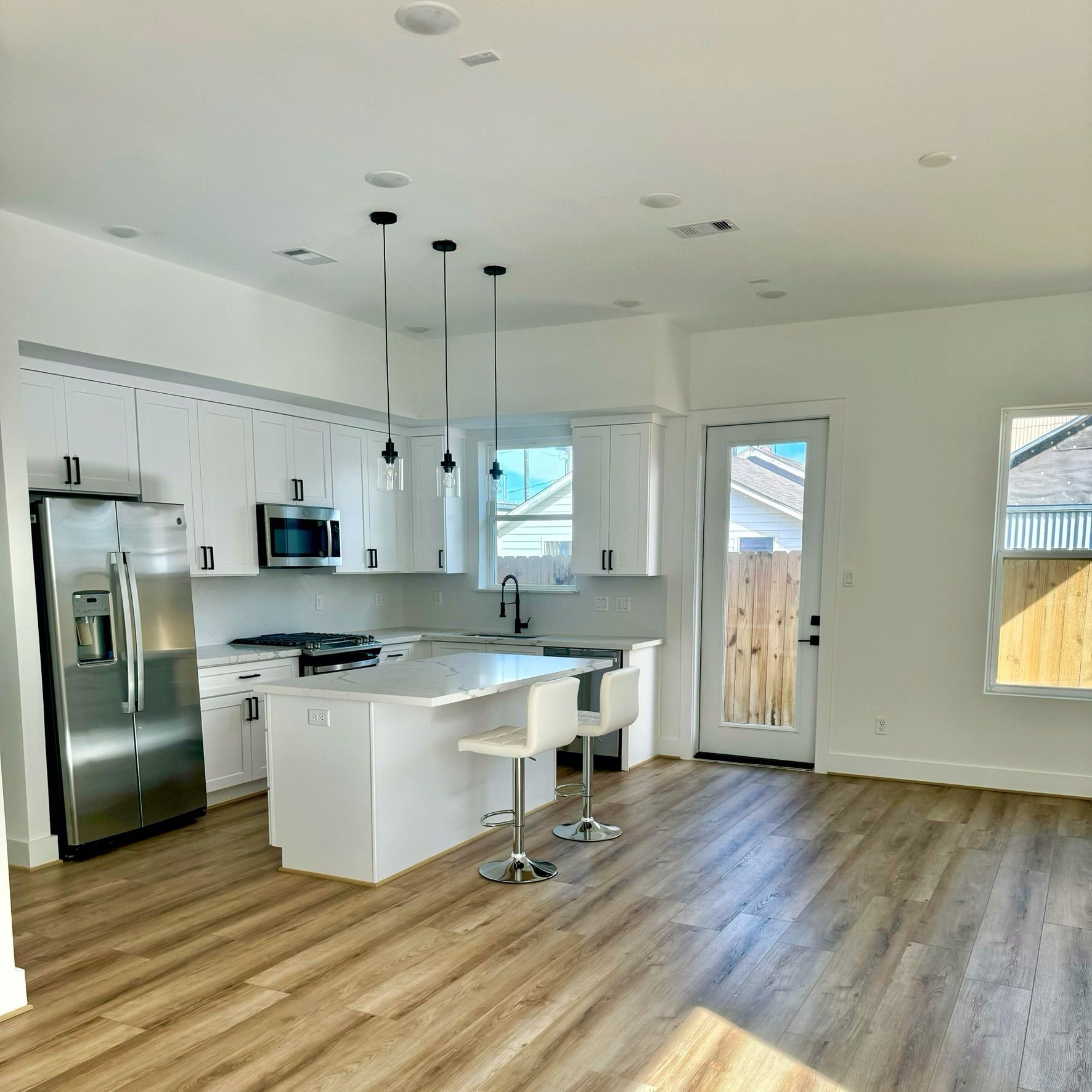 Modern white kitchen with stainless steel appliances, island, and light wood flooring.