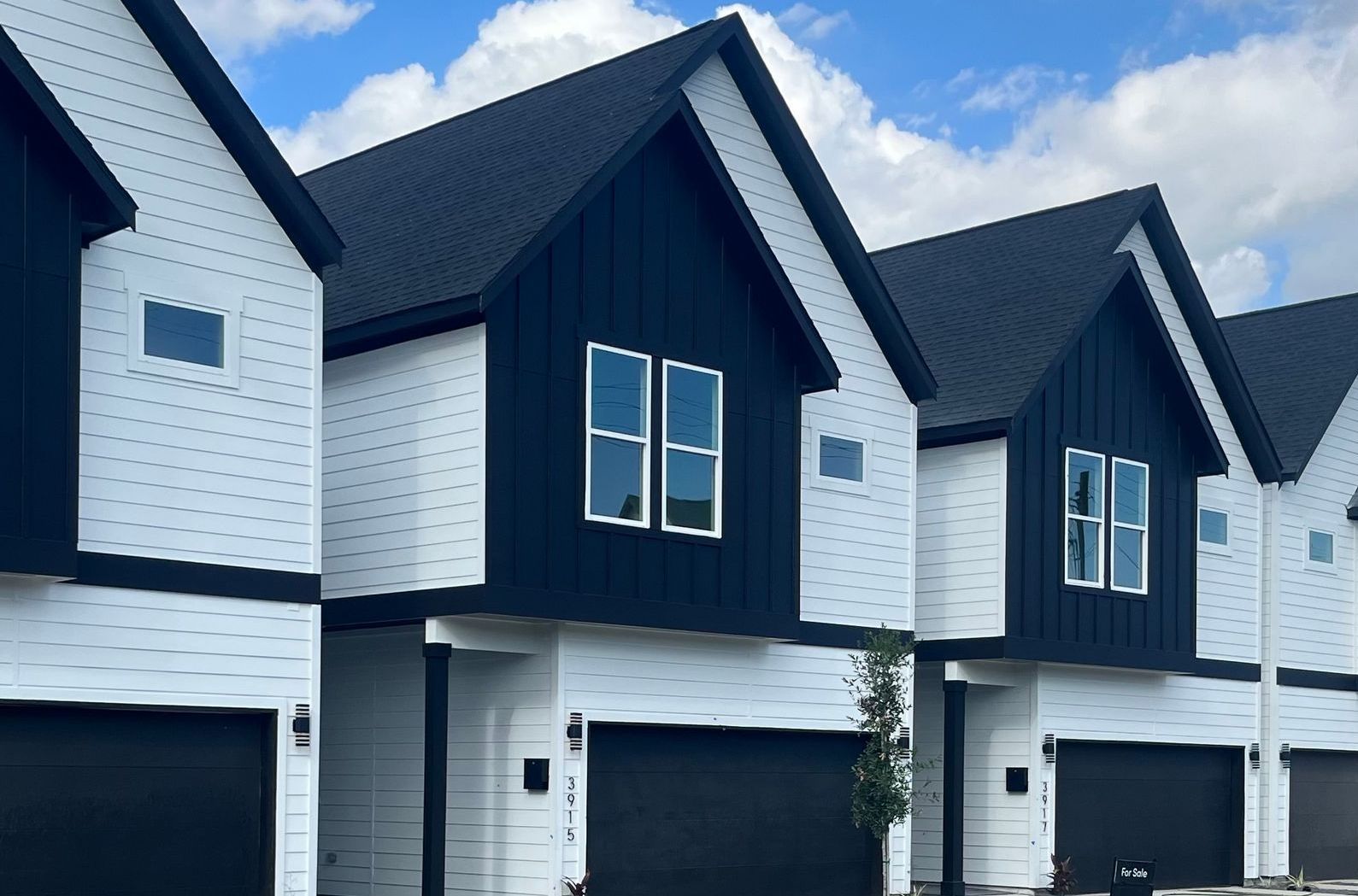 Row of modern townhouses with black and white siding under a blue sky.