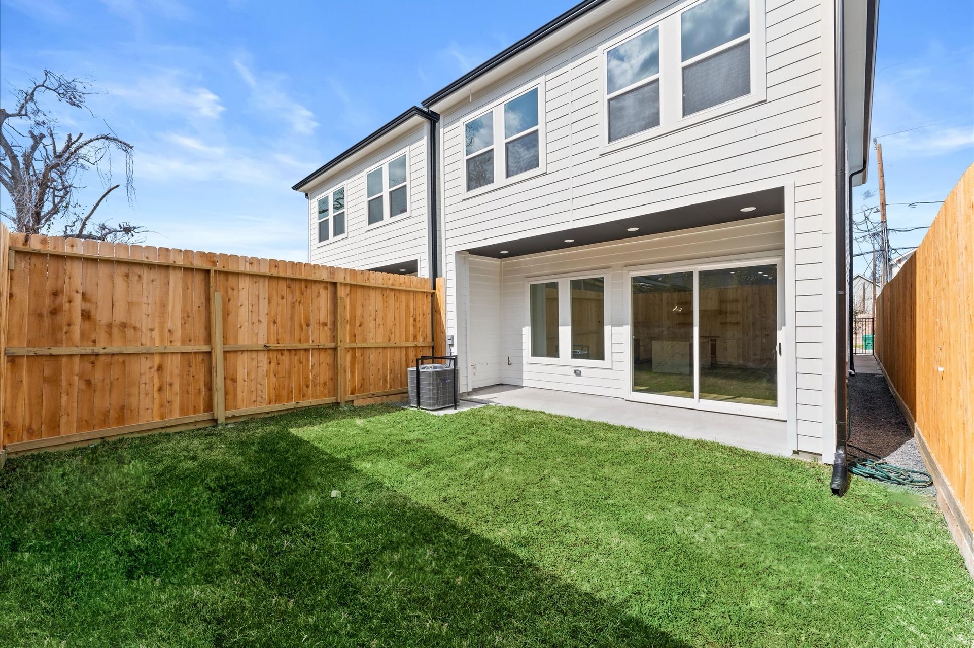 Backyard with green grass, wood fence, and a two-story white house with sliding glass doors.