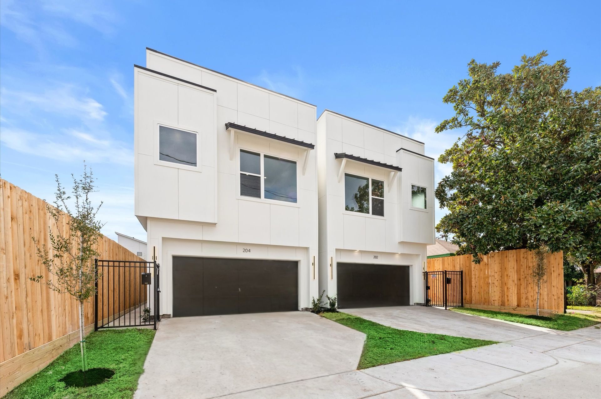 Two-story white modern townhomes with black garage doors, set in a sunny residential area.
