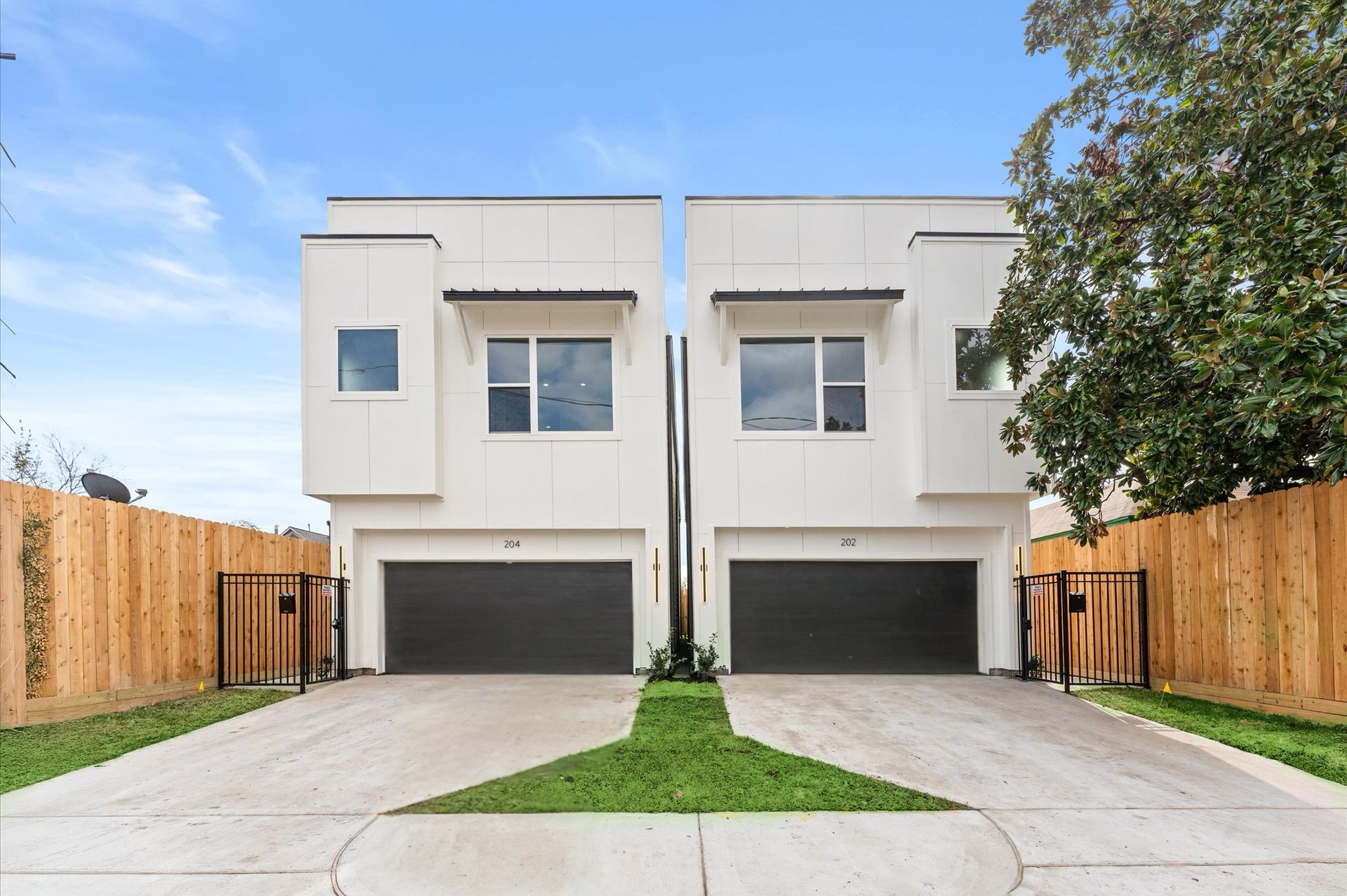 Two modern white townhomes with dark gray garage doors, facing the viewer, on a sunny day.