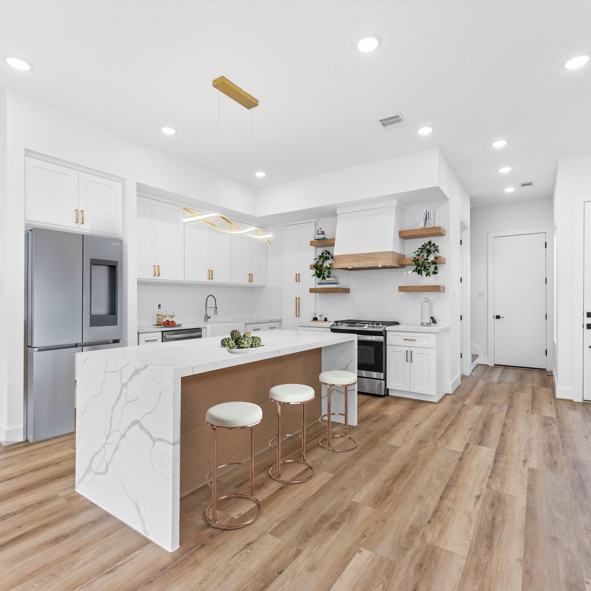 Modern white kitchen with marble island, wood floors, and gold accents.