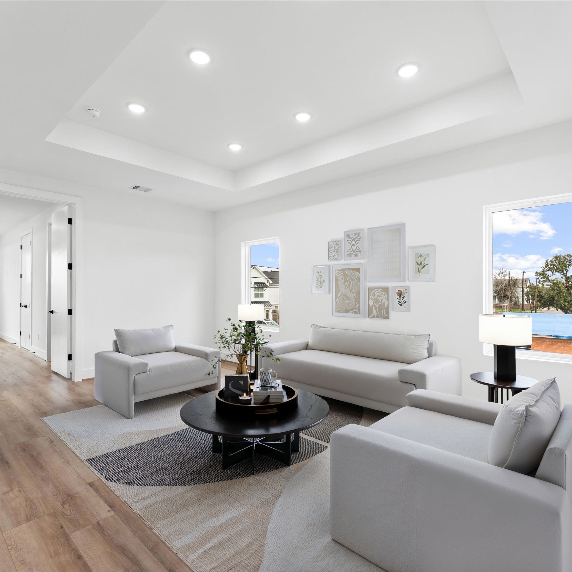 Bright, modern living room with white walls, light furniture, and a black coffee table.