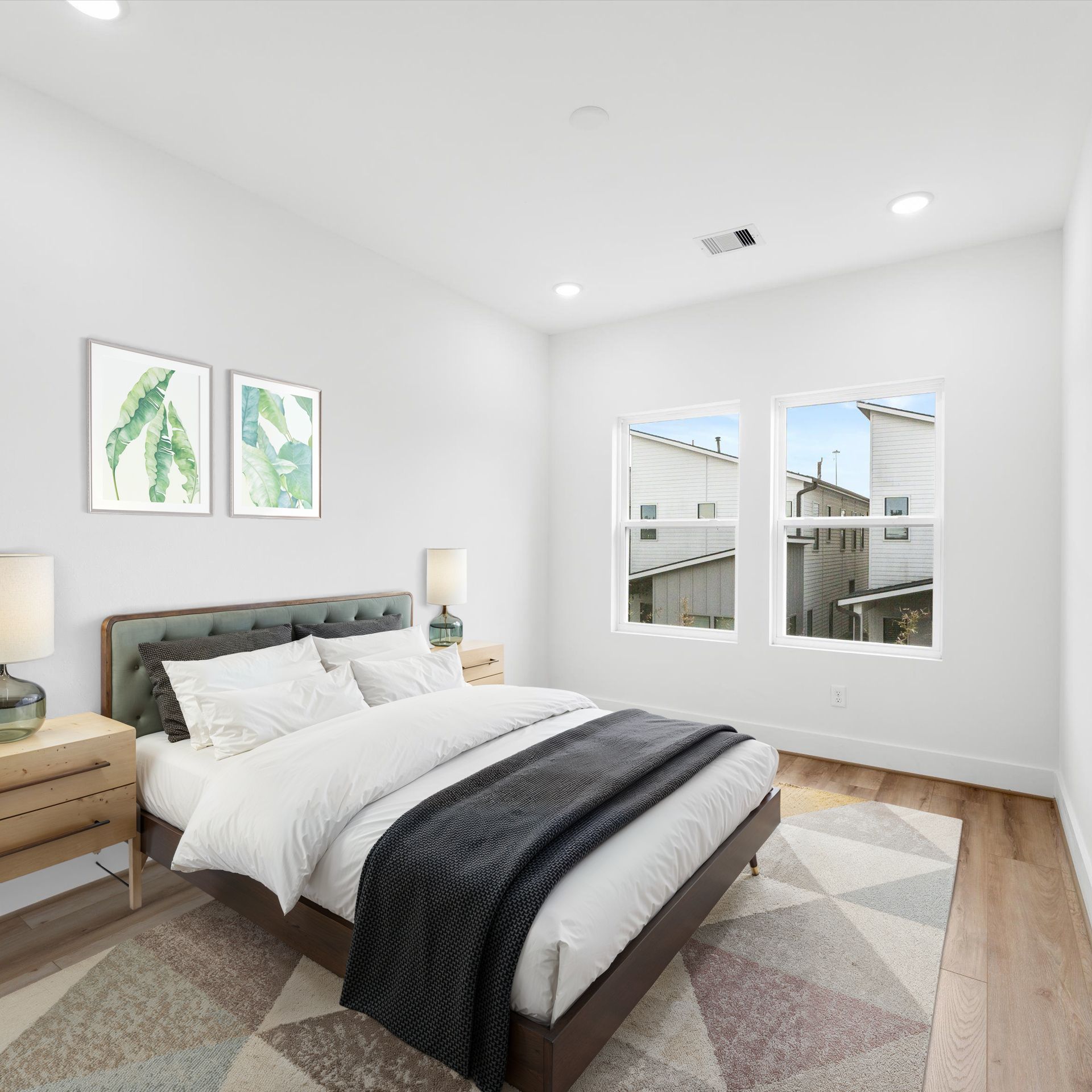 Bedroom with bed, nightstands, art, and a rug. Neutral tones with bright sunlight.