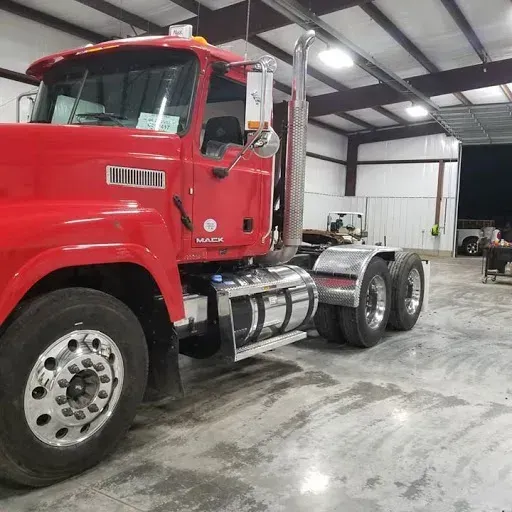Red Mack semi-truck parked inside a garage. The truck has chrome details and a large exhaust pipe.