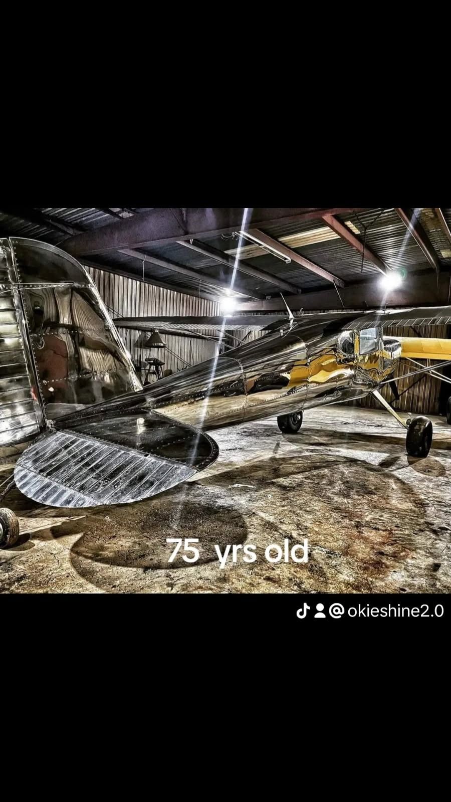A vintage airplane in a dimly lit hangar, 75 years old, with shiny silver and yellow paint.