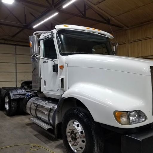 White semi-truck parked in a garage with overhead lighting. The truck has chrome details and a black fender.