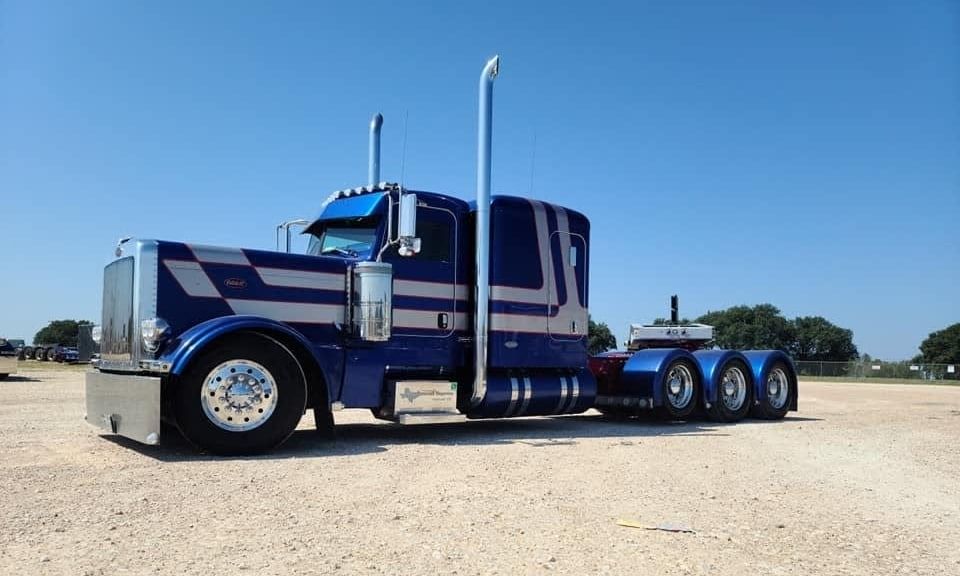 Blue and silver Peterbilt semi-truck parked on gravel under a clear sky.