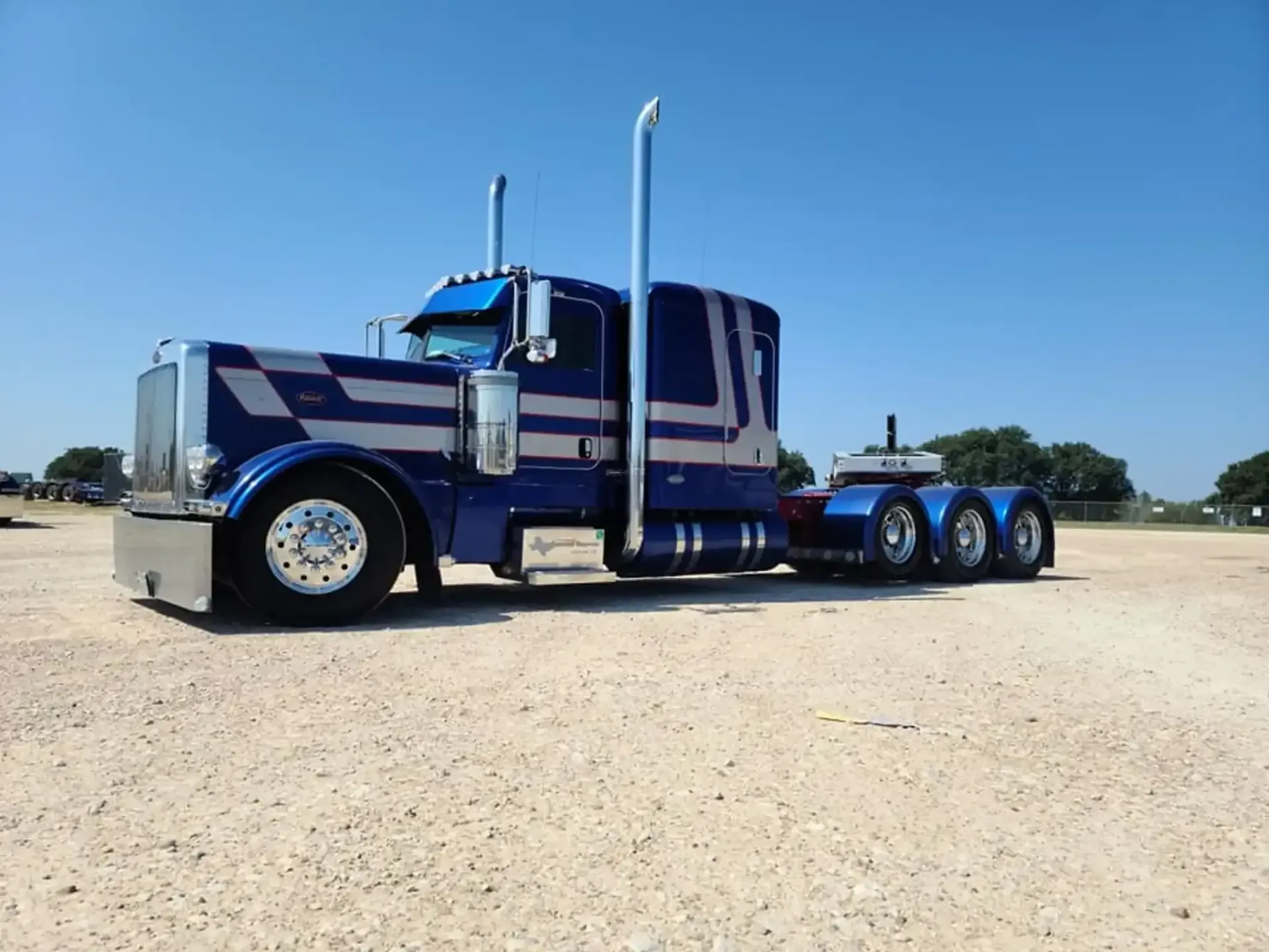 Blue and silver semi-truck on a gravel lot under a clear blue sky.