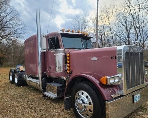 Burgundy Peterbilt semi-truck parked outdoors. Silver details, chrome wheels, and exhaust stack.